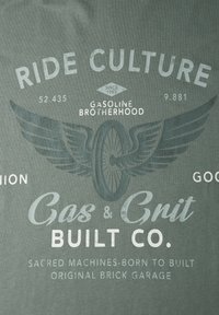 Logo mit einem Motorradreifen mit Flügeln und den Texten „Ride Culture“, „Gasoline Brotherhood“, „Gas & Grit Built Co.“ und „Sacred Machines-Born to Built“.