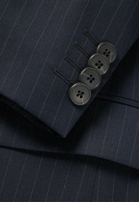 Tessuto per un abito a righe sottili blu navy con una texture liscia, quattro bottoni neri sul polsino con un elegante occhiello, e dettagli di cucitura raffinata.