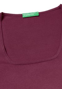Top in cotone borgogna con scollo rotondo. Presenta una texture liscia e un'etichetta verde con la scritta "United Colors of Benetton."