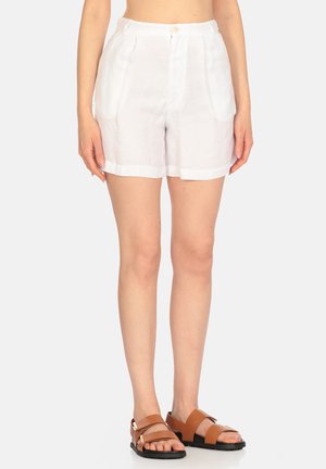 Pantaloni corti bianchi in lino con pieghe, chiusura a bottone e tasche laterali. Abbinati a sandali piatti marroni con design a fascia.