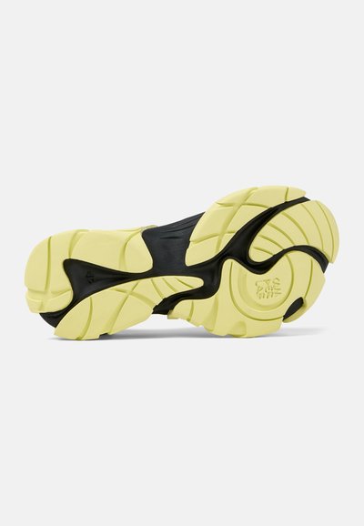 Black and light yellow athletic shoe outsole featuring textured tread patterns, including curved lines and circular accents for grip.