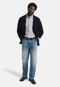 Blazer navy su una camicia a quadri, jeans azzurri chiari e scarpe nere. L'outfit presenta una vestibilità classica con texture e colori diversi.