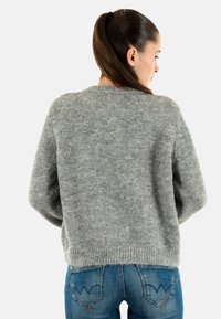 Suéter gris de punto con un corte amplio, cuello redondo y hombros caídos. Tejido texturizado con un acabado suave, llevado sobre unos jeans azules.