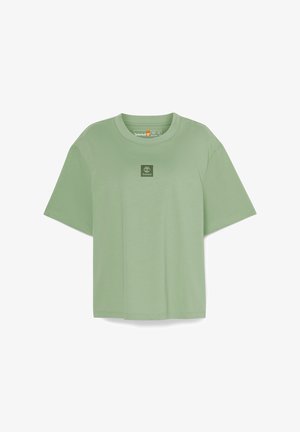 Grön bomullströja med korta ärmar, rund halsringning och en liten fyrkantig logotyp på bröstet. Mjuk textur och lös passform.