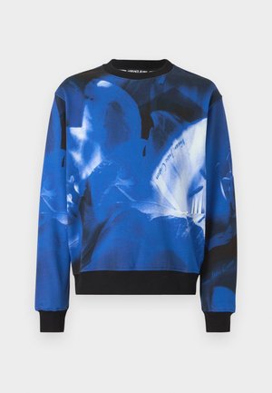 Blå og svart hettegenser med abstrakte blomster mønstre og "Versace Jeans Couture" tekst, med ribbestrikkede mansjetter og kant.