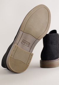 Bottines en daim noir avec semelles en caoutchouc, dotées d'une semelle extérieure texturée de couleur claire et d'accents cousus autour du talon.