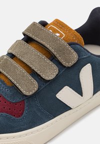 Blaue Wildledersneaker mit Klettverschlüssen, einem Akzent aus braunem Wildleder, einem durchlöcherten bordeauxroten Panel und einem weißen Logo an der Seite.