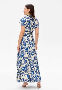 Robe maxi crème avec imprimé floral bleu, manches courtes, ceinture à nouer à la taille, tissu fluide et fente sur le côté au-dessus de l'ourlet.