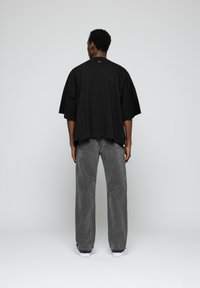 Camiseta negra oversized de manga corta, combinada con jeans grises de corte holgado. Diseño sencillo, textura suave y silueta casual.