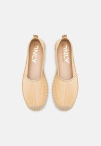 Lysegule espadriller med en vevd tekstur, rund tå og elastisk ankelbånd. Har et gulllogo på innersålen og kontraststing.