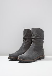 Bottines en daim gris avec un design flou, bout rond et semelle en caoutchouc texturée basse. Coutures contrastées et accents minimalistes.