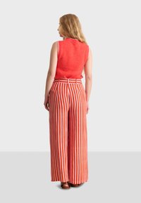 Röd ärmlös topp i texturerad tyg som kombineras med vida byxor i röd och vit rand. Har ett bälte i midjan och en lös passform.