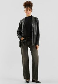 Zwarte leren blazer over een geribbelde zwarte trui, gecombineerd met donkergrijze jeans met wijde pijpen. Accessoires zijn onder andere een ronde tas met studs en zwarte schoenen.