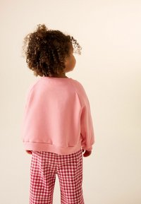 Felpa rosa con polsini a coste, abbinata a pantaloni a quadri rossi e bianchi. Il bambino ha capelli ricci ed è visto di spalle.