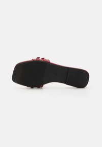 Red leather sandal with a textured upper, adjustable strap, and a black rubber sole featuring horizontal grooves for traction.