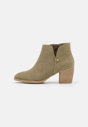 Botte de cheville verte avec une texture tissée, des détails marron et un talon empilé. Présente une ouverture latérale et des accents métalliques subtils.