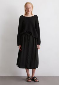 Maglione oversize nero con texture, gonna midi nera fluida con vita regolabile, e sandali neri con fibbie. Design semplice e minimalista.