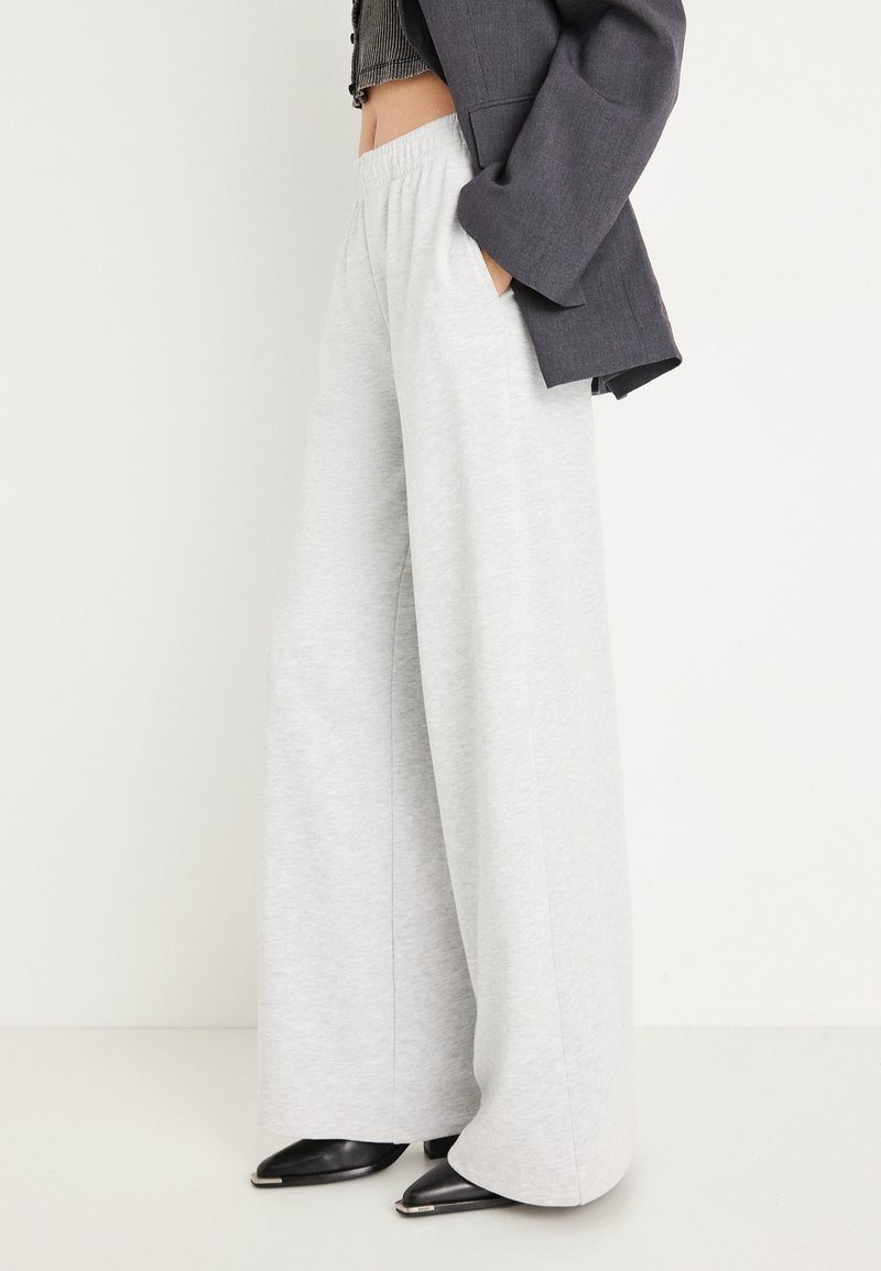 Ανοιχτό γκρίζα φαρδιά φόρμα με απαλή υφή, με ελαστική ζώνη στη μέση και πλαϊνές τσέπες, συνδυασμένα με στενά μαύρα παπούτσια με μυτερή μύτη.