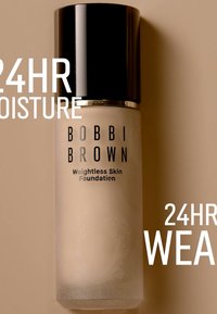 Bobbi Brown Weightless Skin Foundation i glasflaska, frostad finish, svart kork, med fet text som anger fukt och hållbarhet.