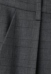Grå rutigt tyg med en texturerad väv som har en blandning av mörka och ljusa gråtoner, som visar vertikala och horisontella linjemönster.