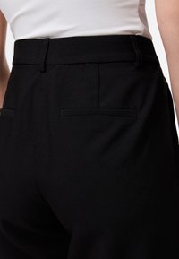 Calças pretas com um design sob medida, textura suave, bolsos frontais planos e uma cintura de altura média.