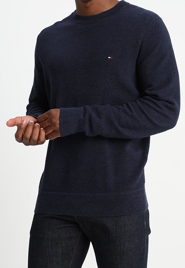 Maglione lavorato a maglia blu navy con texture a coste, scollo rotondo e maniche lunghe. Presenta un piccolo logo rosso e bianco sul petto.