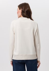 Lichtbeige sweatshirt met lange mouwen, subtiele naaddetails en een rechte snit, gecombineerd met donkerblauwe jeans. Katoene textuur.