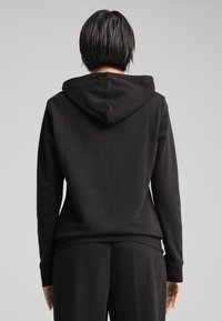 Black hoodie with a kangaroo pocket and adjustable drawstring. Features a smooth texture and ribbed cuffs, paired with matching pants.