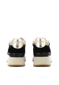 Baskets en suede noir avec des accents dorés, talon texturé, et une semelle en caoutchouc blanc avec un motif. Marque sur le talon.
