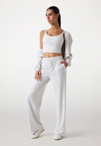 Vitt sportigt outfit med en fitted crop top och lösa byxor med snörning. Mjuk tyg, minimalistisk design med logotypdetaljer. Vita sneakers.