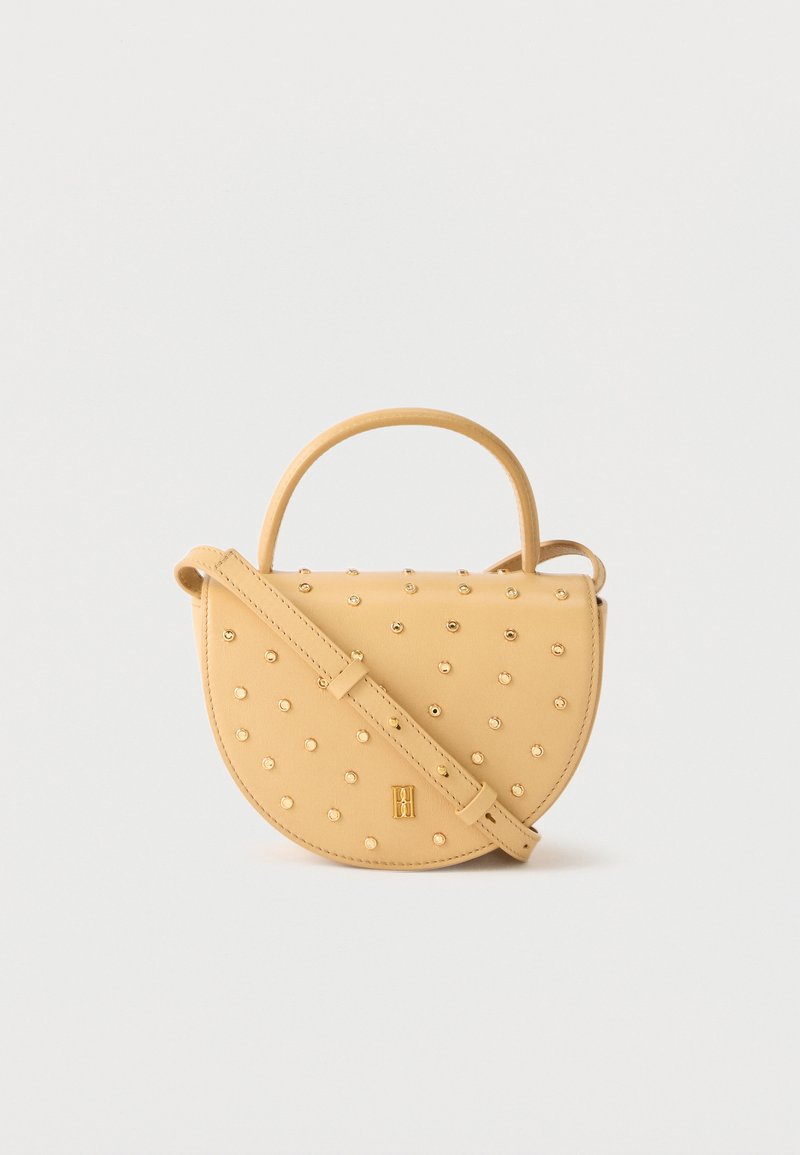 Κίτρινη ημικυκλική τσάντα χειρός με χρυσά καρφιά, κοντή λαβή και ρυθμιζόμενο λουρί ώμου σε απλό φόντο.