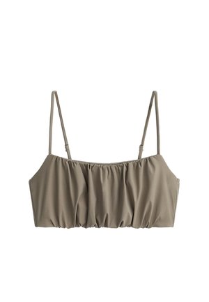 Femme portant une tenue deux pièces taupe avec un top court et un pantalon large, associée à des baskets noires, debout sur un fond gris.