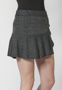 Minifalda de cuadros en negro y gris con un dobladillo acampanado, tejido texturizado y cintura ajustada. Los patrones incluyen pata de gallo y cuadro.