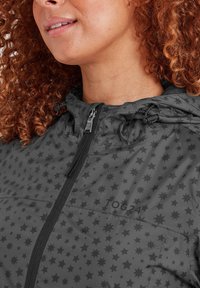 Woman with curly red hair wearing a gray hooded jacket patterned with black stars and a front zipper.
