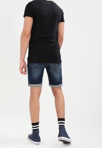 Camiseta oscura combinada con pantalones cortos de denim oscuro, con los dobladillos enrollados, mostrando un ajuste slim. Se lleva con zapatillas azul marino y calcetines a rayas. Diseño sencillo.