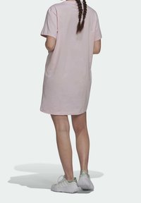 Růžové bavlněné šaty ve stylu trička s krátkým rukávem, volný střih, ke kolenům, doplněné o světle zbarvené sportovní boty. Hladký povrch, bez vzorů.