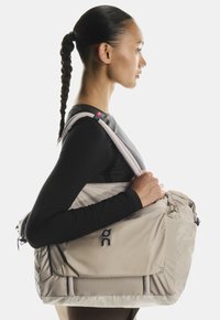 Bežna sportska torba s teksturiranim materijalom, ističe logotip, ima dvostruke uže ručke i bočnu džep sa zatvaračem.