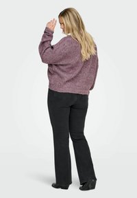Lila strukturierter Pullover mit lockerer Passform, Rundhalsausschnitt und abfallenden Schultern, kombiniert mit schwarzen Schlagjeans und schwarzen Schuhen.