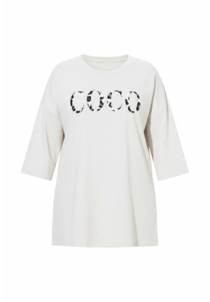 Hvid oversized t-shirt med korte ærmer med sort og brun plettet "COCO" grafisk tryk. Blødt bomuldsstof, afslappet pasform.