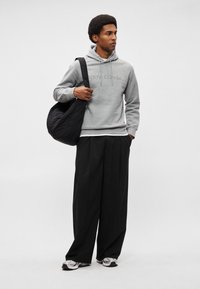 Felpa grigia con logo, borsa a spalla nera, pantaloni larghi neri e sneakers grigie/nere. Tessuto morbido, vestibilità rilassata.