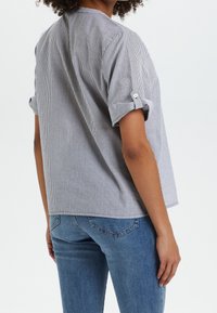 Randig kortärmad skjorta i svart och vitt, med uppvikta ärmar och avslappnad passform. Matchad med ljusblå denimjeans.