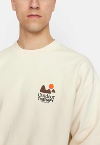 Crème-kleurige sweatshirt van zachte katoen, met een grafische logo van bruine bergen en een kleurrijke zonsondergang. Ribbelband bij de hals.