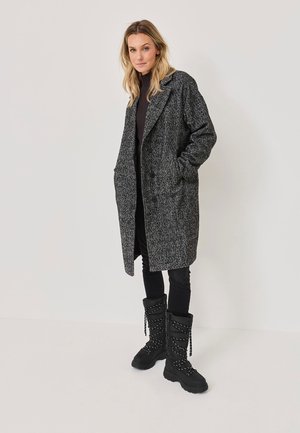 Manteau gris texturé avec un col cranté, des poches avant et des boutons, associé à des bottes noires à lacets épaisses et un pantalon noir slim.