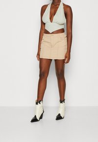 Halter top v světle modré a bílé kostkované, doplněný béžovou mini sukní s kapsami. Černé a bílé kožené kotníkové boty ve stylu kovboje.