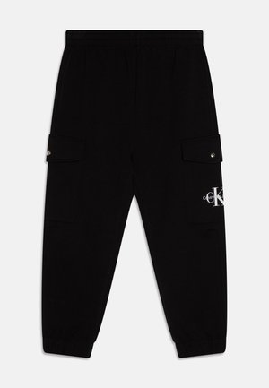 Czarne spodnie dresowe z elastycznym paskiem i mankietami, boczne kieszenie cargo na zatrzaski oraz białe logo Calvin Klein na kieszeni na prawym udzie.
