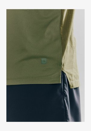 Olive green, short-sleeved shirt with a textured, breathable fabric. Features a small, green logo badge and a side slit for ease of movement.