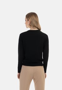 Maglione nero con maniche lunghe e orlo a coste, mostrato dal retro. Tessuto liscio con un design semplice e classico. Abbinato a pantaloni beige.