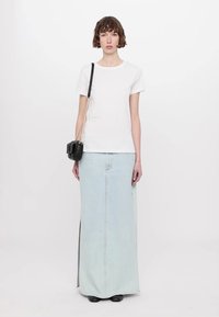 Tricou alb din bumbac asortat cu o fustă lungă din denim de culoare bleu deschis, cu o fanta frontală și cusături contrastante. Geantă crossbody neagră cu curea din lanț.