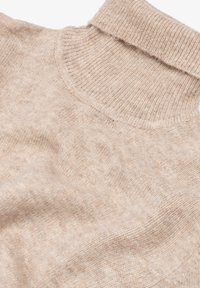 Maglione in cashmere beige con colletto arrotolato, caratterizzato da una superficie morbida e texturizzata e un aspetto rilassato e drappeggiato.
