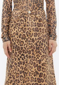 Gonna di jeans con stampa leopardata, vita alta, tasche anteriori e un taglio leggermente svasato. Motivo marrone e nero su uno sfondo beige.